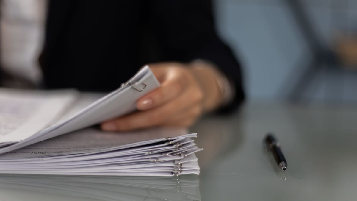 A person holds a stack of paper documents on a desk.