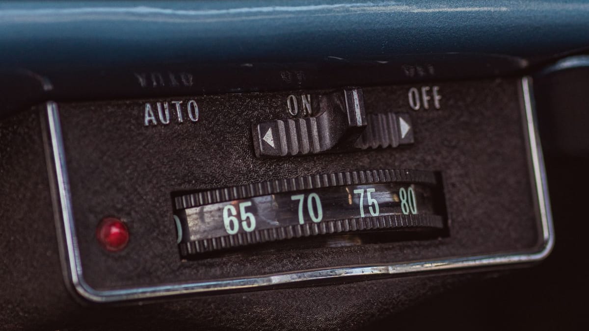 A close-up of a vintage dashboard control panel with labeled switches, dials, and a red indicator light.