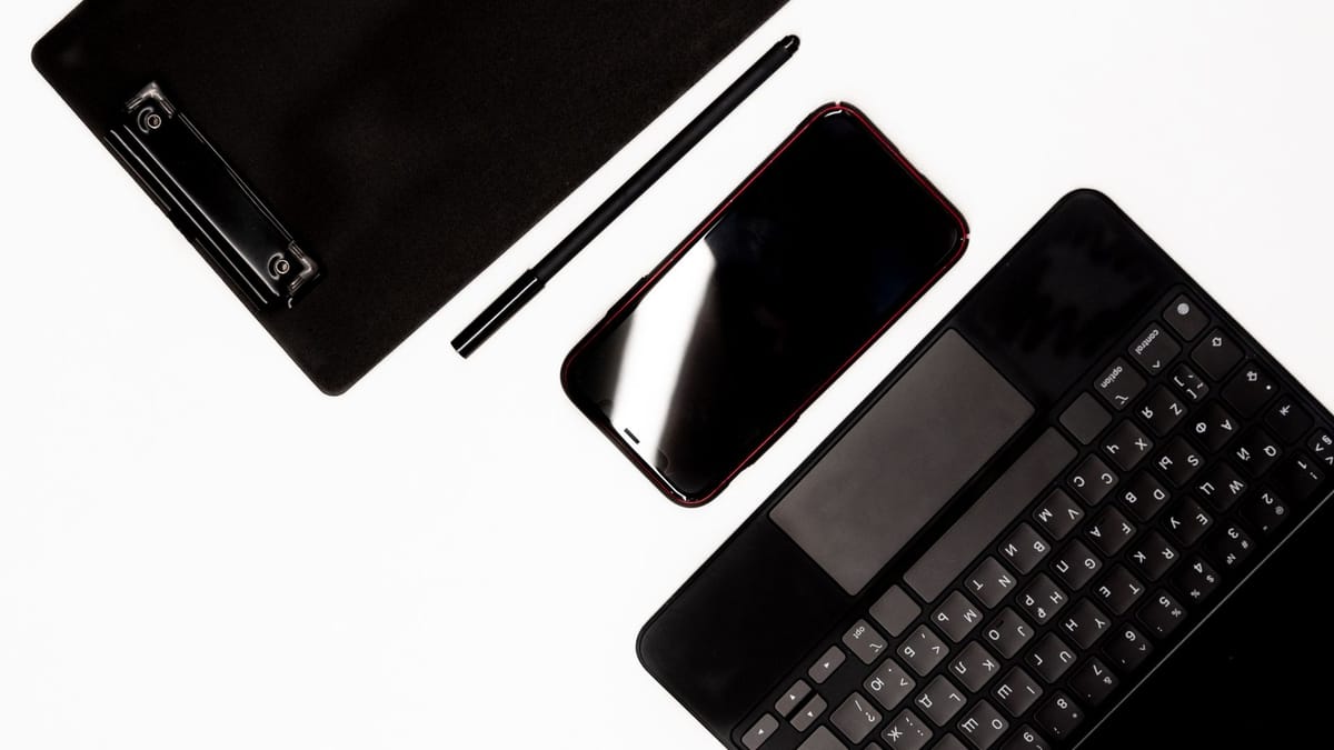 A smartphone, keyboard, pen, and clipboard arranged on a white work surface.