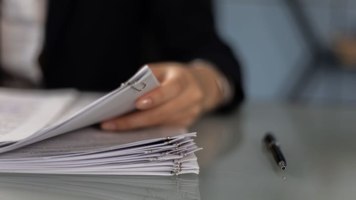 A person holds a stack of paper documents on a desk.