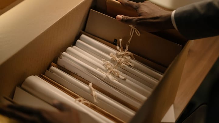 Hands organize file folders and bundled documents inside a cardboard box.