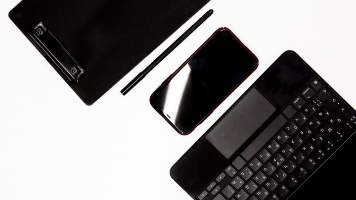 A smartphone, keyboard, pen, and clipboard arranged on a white work surface.