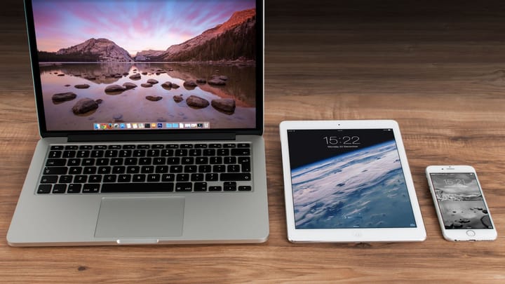 A laptop, tablet, and smartphone arranged on a wooden desk.