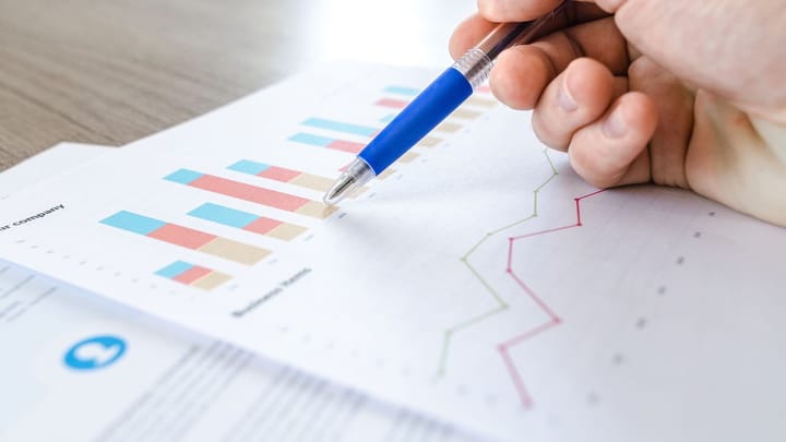 A hand holds a pen over a printed spreadsheet with charts and survey data.